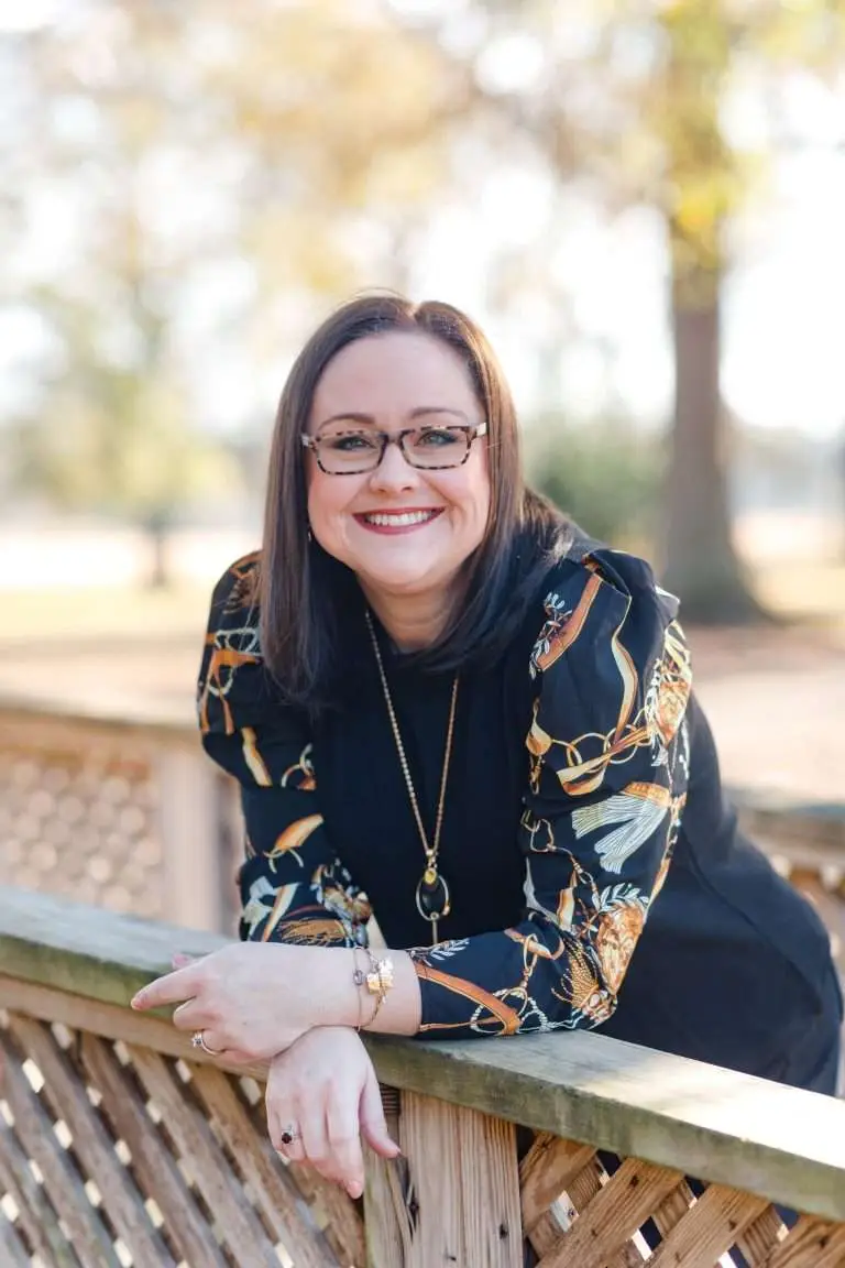 Amanda Jones, smiling and leaning on a wooden fence on a sunny day.